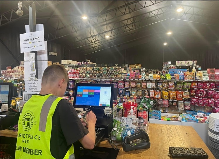 A CitiSkills participant in a CitiReach hi-vis vest serving a customer at the checkout counter